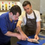 A trainee from The CRUMBS Project fillets a fish with a chef from Rick Stein Sandbanks