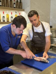 A trainee from The CRUMBS Project fillets a fish with a chef from Rick Stein Sandbanks