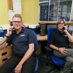 Lee and Ursula from The CRUMBS Project sit on chairs in an office using the new telephones supplied by T2K Voice & Data