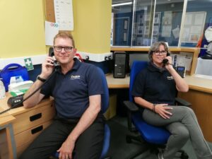Lee and Ursula from The CRUMBS Project sit on chairs in an office using the new telephones supplied by T2K Voice & Data
