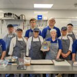 Trainees and staff pose with a Craft Guild of Chefs' plaque in the training bakery at The CRUMBS Project
