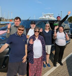 A group of trainees and staff stand smiling at the ferry port in Lymington