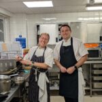 A volunteer female chef and a male chef stand in the training kitchen at The CRUMBS Project training centre