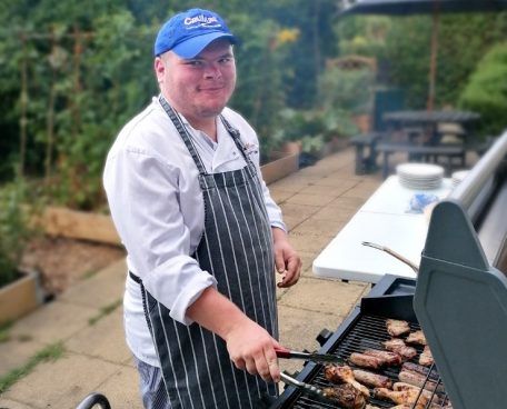 A trainee cooking on a barbecue in the kitchen garden at Crumbs