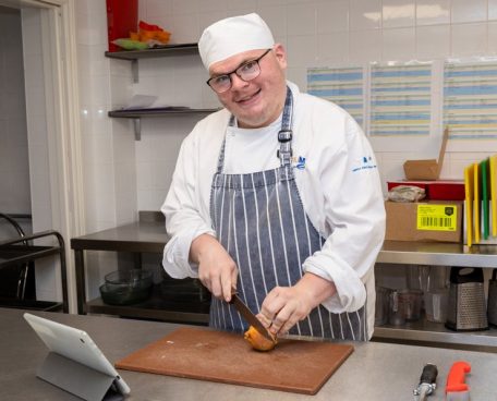 A trainee in a chef’s uniform in the training kitchen