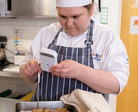 A trainee using a thermometer in the training kitchen