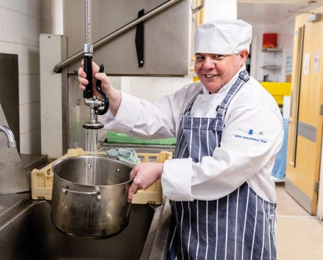 A trainee washing up a pot at a sink in the training kitchen