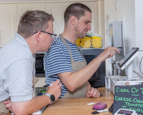 Two trainees at work using the till at a cafe